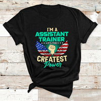 Black T-shirt with chest text-and-eagle graphic reading “I’m a Assistant Trainer… Greatest Power.”