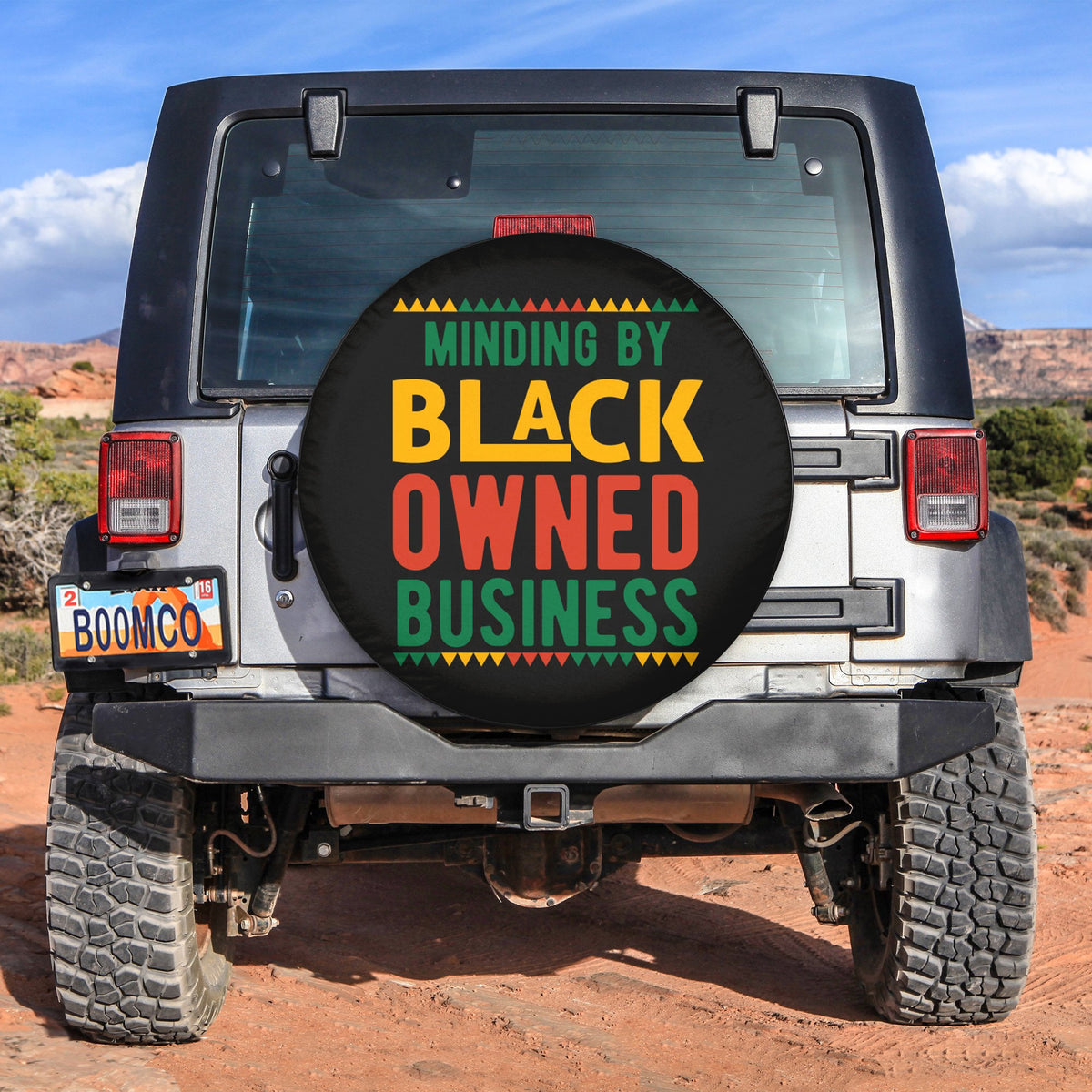 Spare tire cover with circular multicolor text: Minding By Black Owned Business