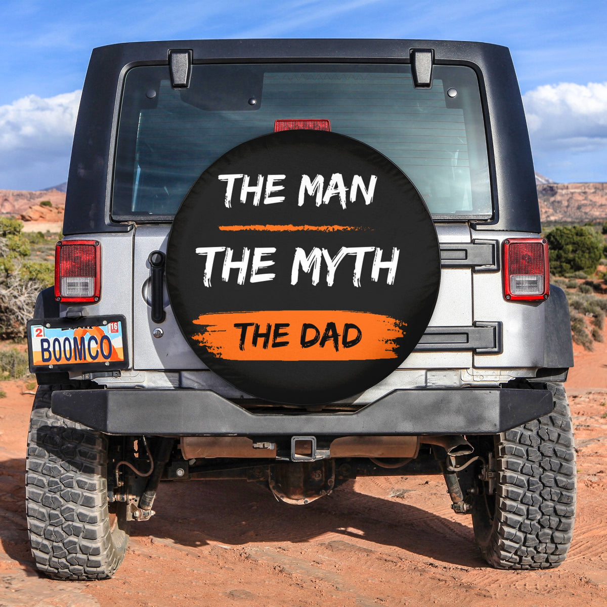 Round black spare tire cover with bold text "THE MAN THE MYTH THE DAD"