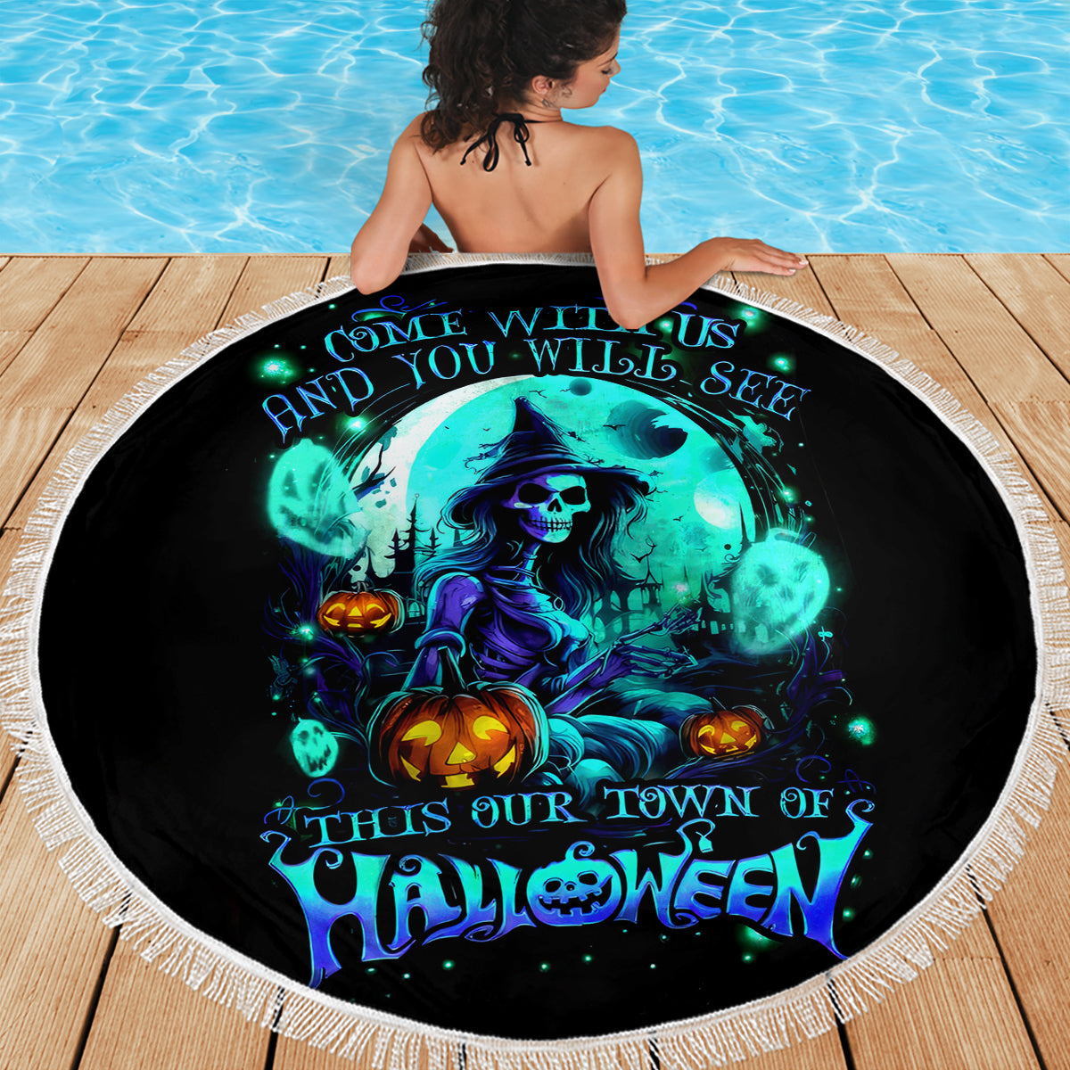 Round black Halloween beach blanket with blue witch skull graphic and white fringe, on deck