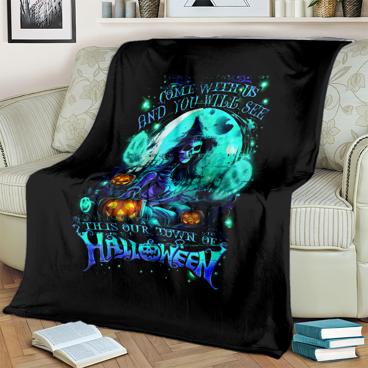 Black Halloween blanket with neon teal skull-and-witch artwork, placed on bed