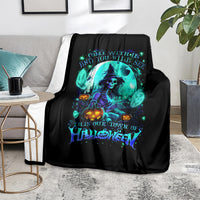 Black Halloween throw blanket with neon teal skull-and-witch design, laid on rug
