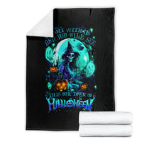 Black Halloween blanket with teal skull-and-witch graphic, folded with rolled white towels