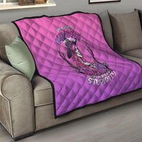 Pink quilt with diamond pattern and witch-skull graphic draped over a sofa