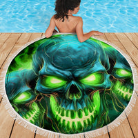 Round beach blanket with green-blue skull artwork and white fringed border on wood