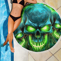 Round beach blanket with glowing green-blue skull graphic and white fringed edge by water