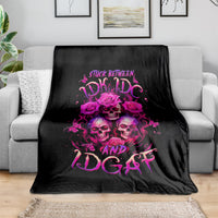 Black skull graphic throw blanket with pink roses and lettering, draped over sofa.