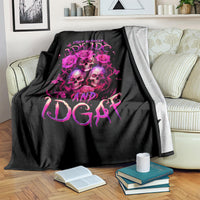 Black skull graphic blanket with pink roses and lettering, draped on striped sofa back.