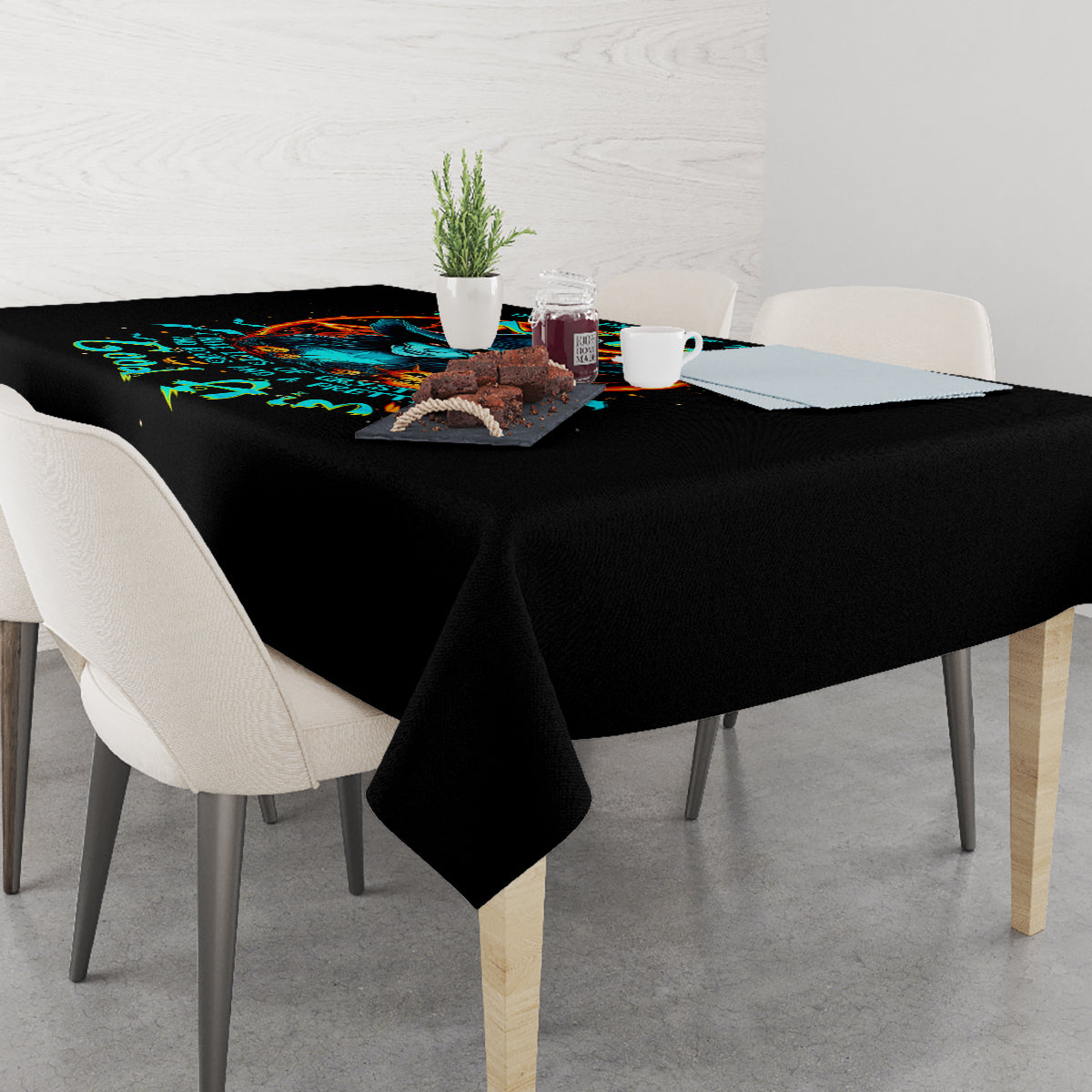 Black tablecloth with colorful witch skull artwork, spread across a dining table