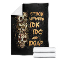 Folded black skull graphic blanket with gold skull artwork and text, beside stacked white towels