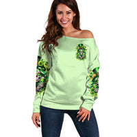 Light green off-shoulder sweater with chest emblem and skull-themed sleeve graphics