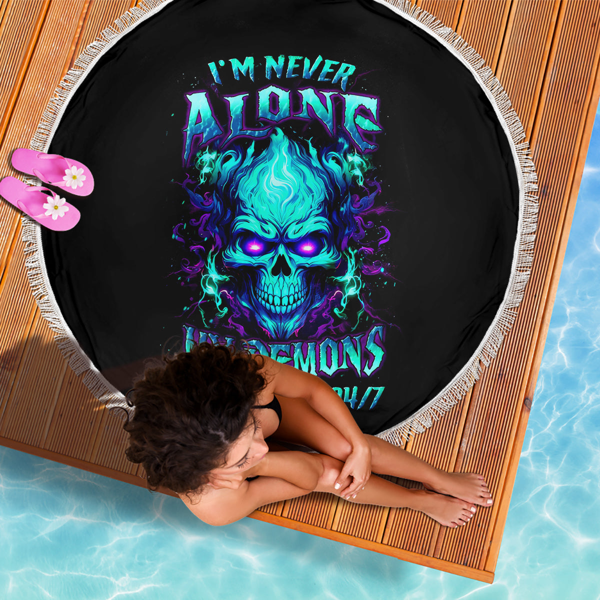Black round beach blanket with fringe, blue skull graphic and neon text on it