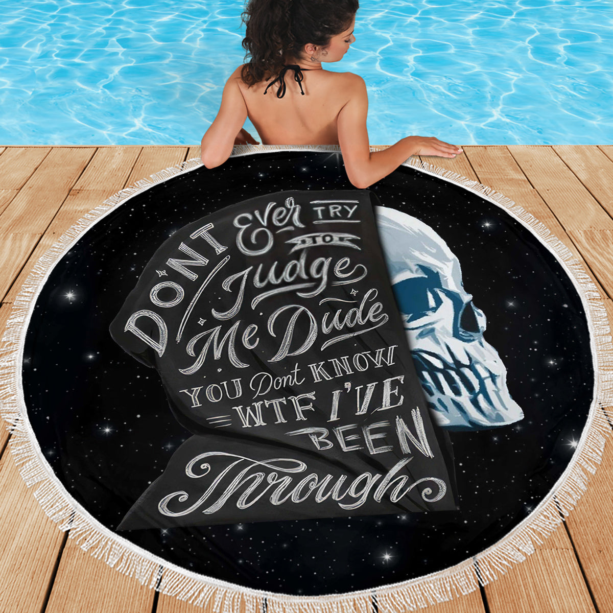 Black round beach blanket with skull graphic, spread flat on deck with fringes