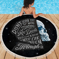 Black round beach blanket with skull graphic, spread flat on deck with fringes