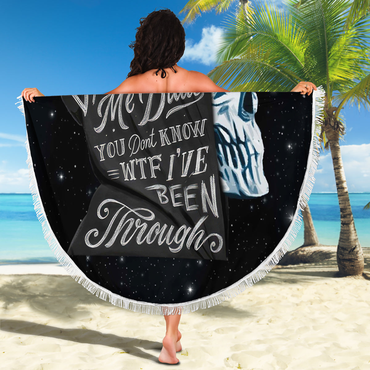 Black round beach blanket held outdoors, skull portrait with fringed white border