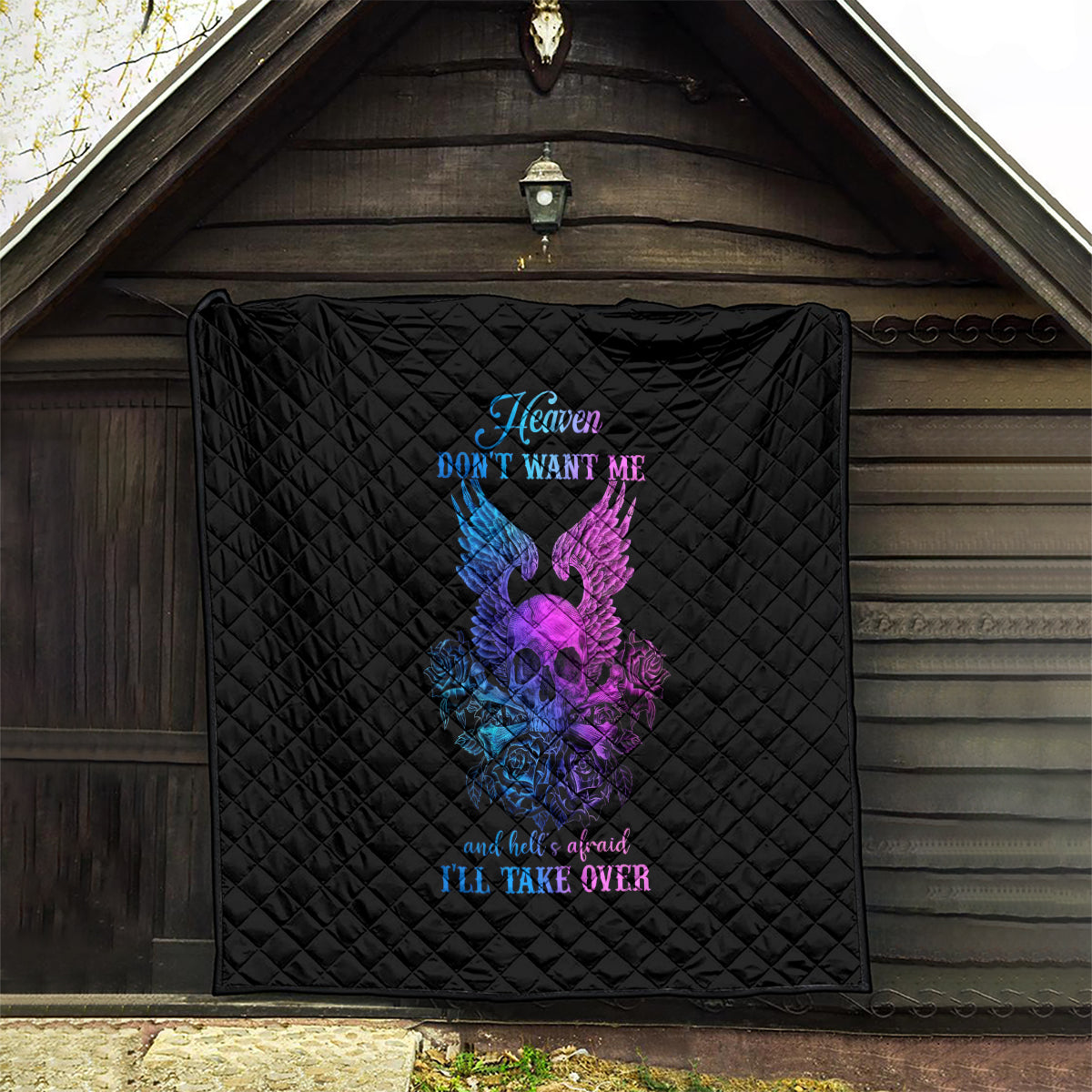 Black quilt blanket with diamond quilting and purple/blue winged skull graphic on porch
