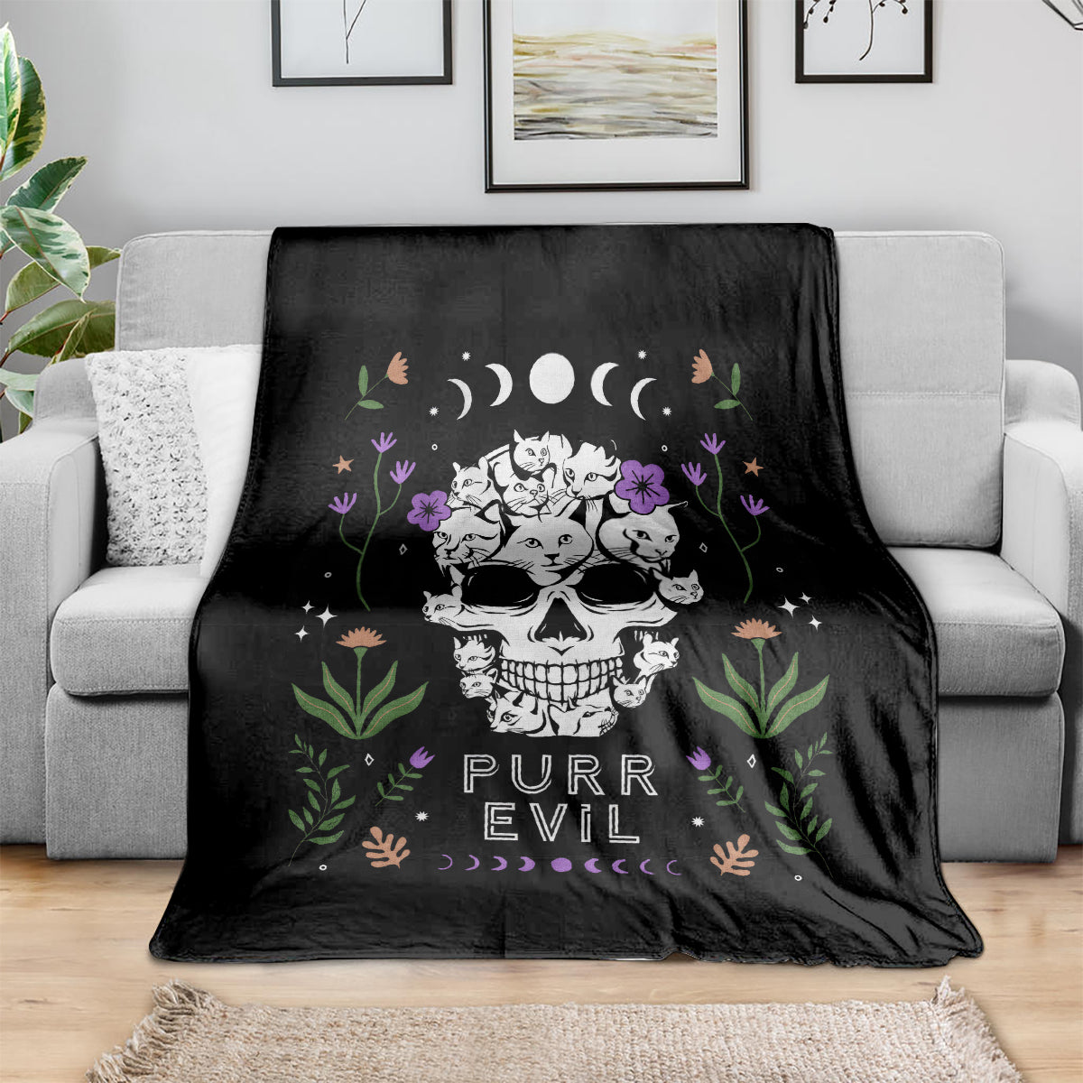 Black cat skull blanket on light sofa with cats, flowers, moons, and 'PURR EVIL' design