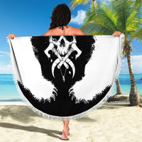 Black-and-white round beach blanket held up, showing bear skull cross design with fringe