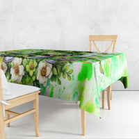Green floral watercolor tablecloth draped over wooden dining table, long overhang