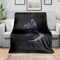 Black blanket draped over light gray sofa, featuring blue grim reaper skeleton and scythe