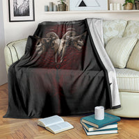 Black skull-and-wings blanket with red central design, draped over striped sofa seat.
