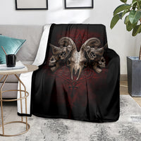 Black skull-and-wings throw blanket with red central emblem, spread over gray couch.