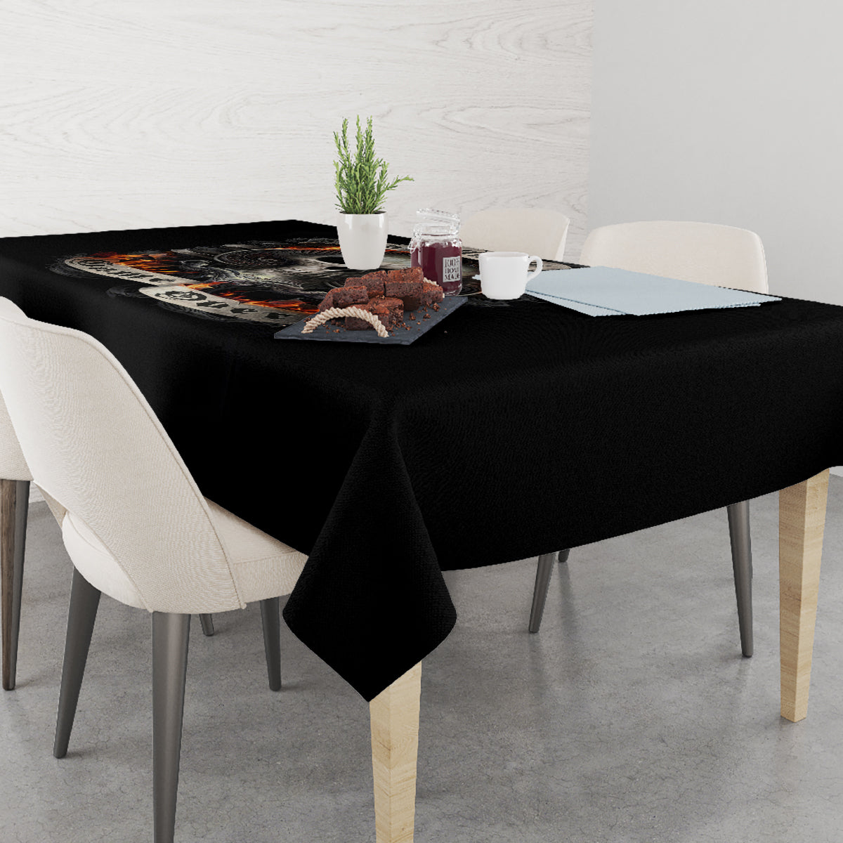 Black tablecloth with skull flame design, laid over dining table with cups.