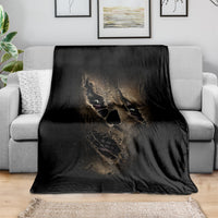 Black throw blanket with mummy face skull print, spread over a gray couch