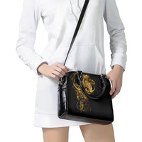 Black shoulder bag with gold warrior crest and long strap, worn on arm