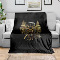 Black blanket featuring golden steampunk skull and wings emblem, laid on a gray couch