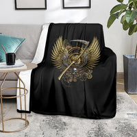 Black blanket with golden steampunk skull and wing emblem, folded over a sofa seat