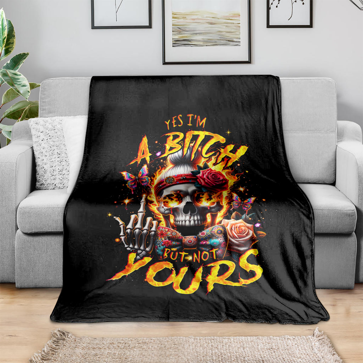Black skull graphic blanket with roses and bold text, laid over grey couch