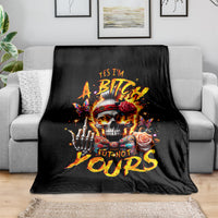 Black skull graphic blanket with roses and bold text, laid over grey couch