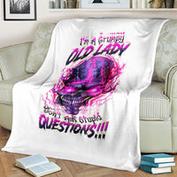 White skull graphic blanket draped on couch, featuring purple-pink skull and slogan text