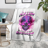 White skull graphic blanket folded on sofa, showing neon purple-pink skull and text