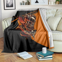 Black and orange skull with wings graphic blanket on a bed with books nearby