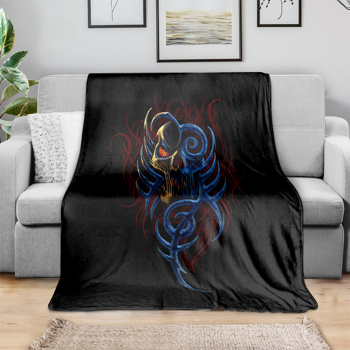 Black blanket with blue devil skull scream design, spread over gray sofa cushions