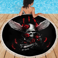 Round black beach blanket with winged skull and red rose graphics, bordered by fringe.