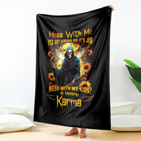 Black graphic blanket hanging display, showing hooded skull figure, sunflowers, and orange text