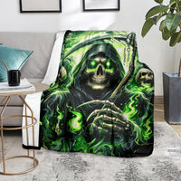Green flame skull reaper blanket with skeleton hand and skull face, laid on gray sofa