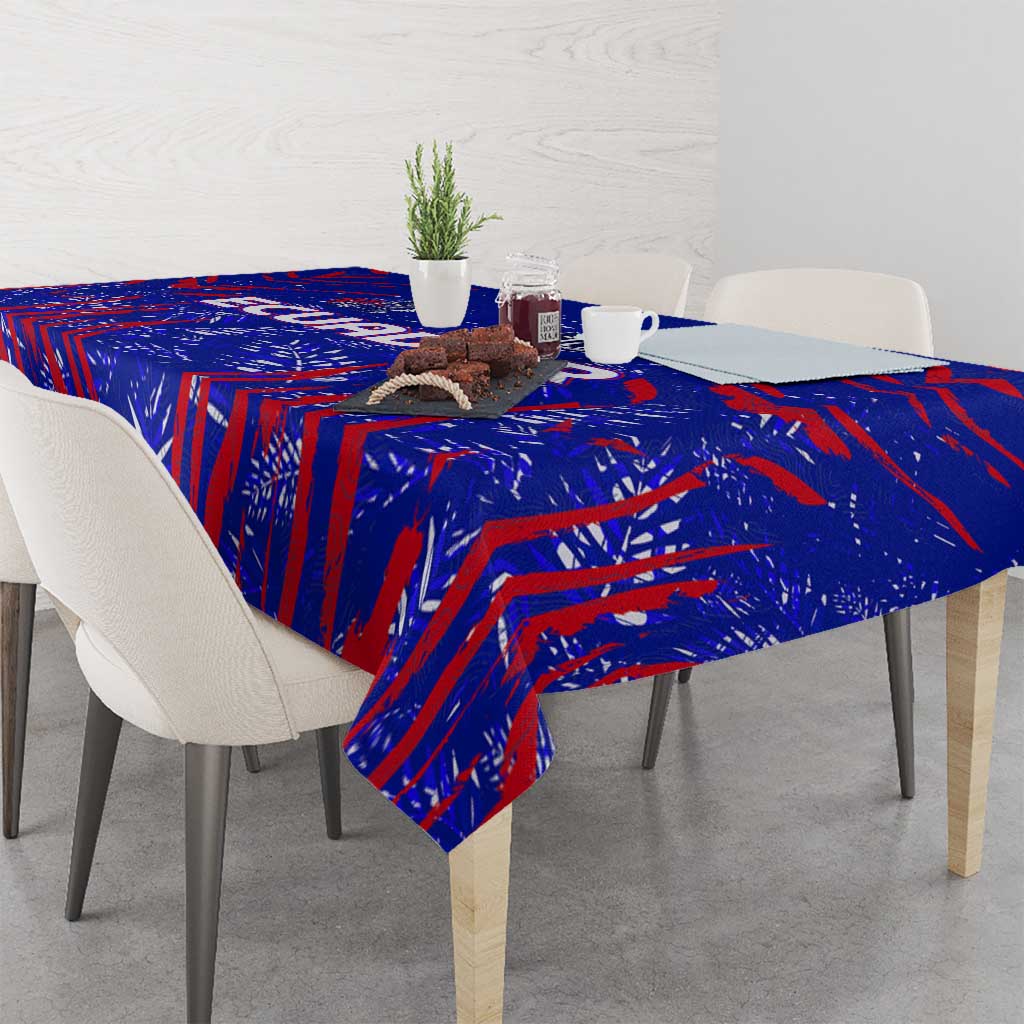 Blue tablecloth with red pattern spread across dining table, cups and vase on top