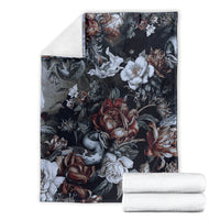 Dark skull and snake floral throw blanket with roses and white flowers, stacked with folded textiles