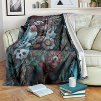 Green-themed blanket with dark floral and eye motif, draped on cream sofa beside books