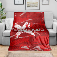 Red Switzerland football blanket spread on gray sofa, showing winged trophy and star