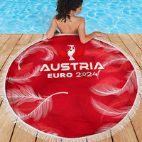 Red round beach blanket with white fringe and Austria Euro 2024 graphic, on wooden deck