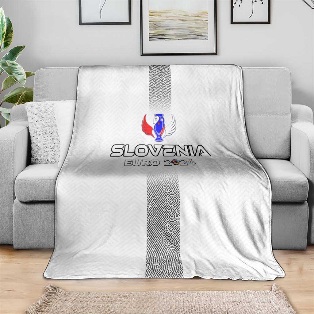 White Slovenia blanket on gray sofa, featuring crest logo and dark center stripe