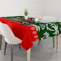 Tablecloth draped on a dining table with green tropical holiday print and red edge