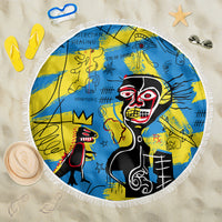 Round fringed beach blanket with blue-yellow psychedelic skull figure artwork.