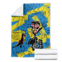 Folded blue and yellow psychedelic skull-face art blanket with stacked white towels