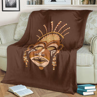Brown tribal face print blanket, draped on a couch with books on the floor